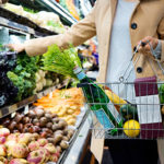 panier en métal de courses rempli de légumes verts avec une personne se servant dans le rayon légumes